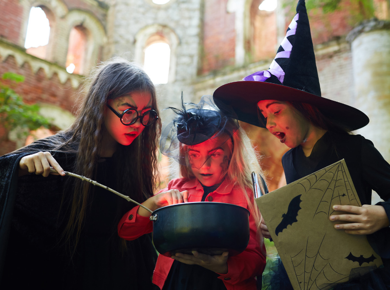 Dzieci przebrane za czarodziejki w spiczastych kapeluszach mieszają magiczny wywar w kociołku